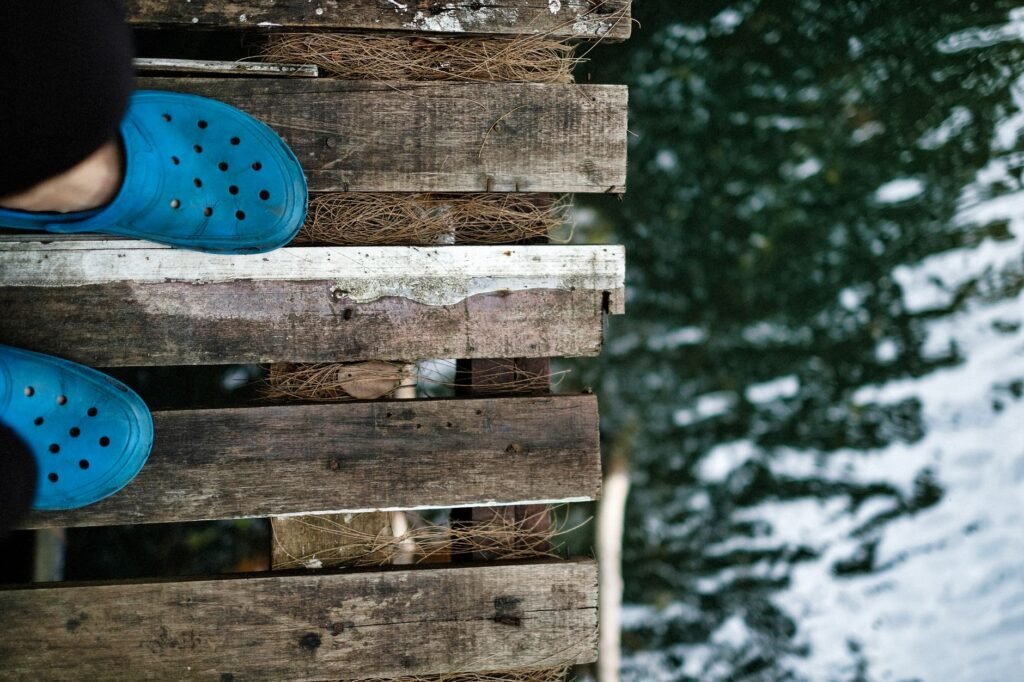 Close-up of feet in blue shoes on a wooden bridge above water.