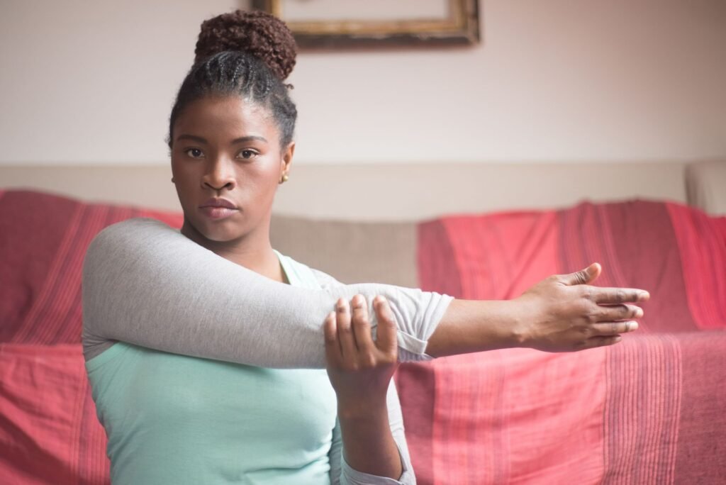 An African American woman performs an arm stretch exercise indoors with focus and determination.