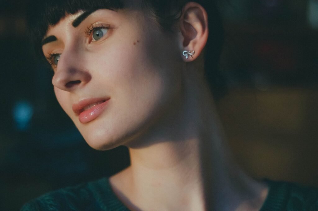 Close-up portrait of a thoughtful young woman with short hair and earrings in dim lighting.